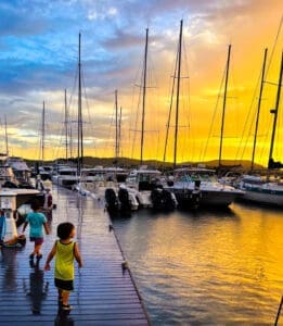 A group of people walking on the dock near boats.