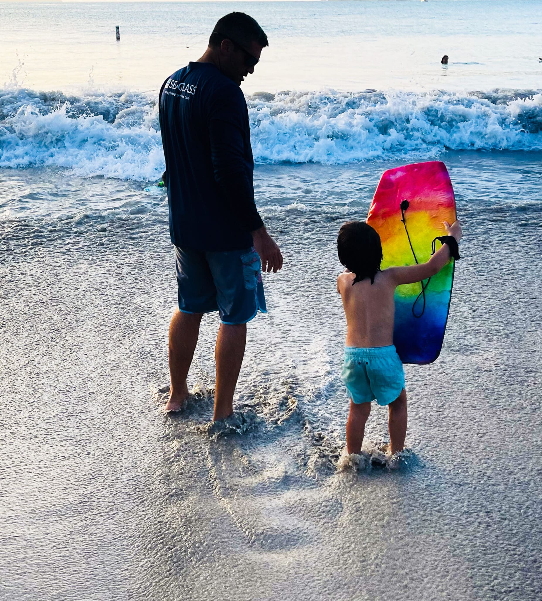 A man and child in the water with a boogie board.