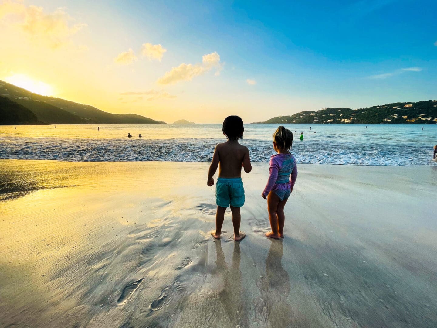 Two children standing on the beach at sunset.