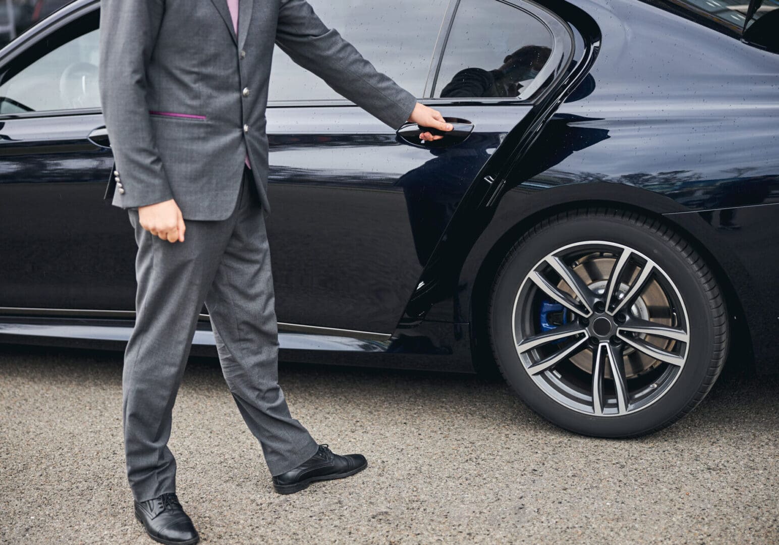 Cropped photo of a driver in a stylish suit opening the car door for his passenger
